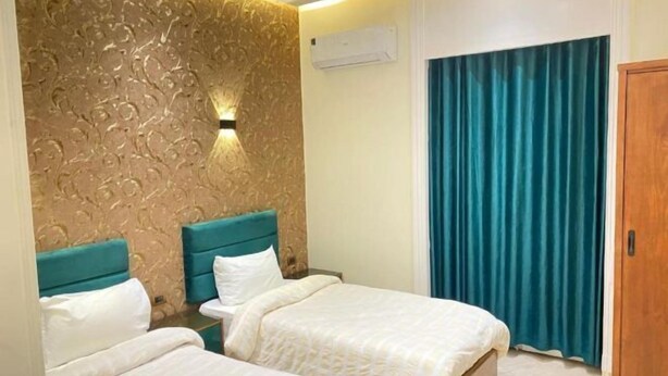 A hotel room with two beds, a textured wall, an air conditioning unit, and a blue curtain. - Richmond Hotel (Cairo)