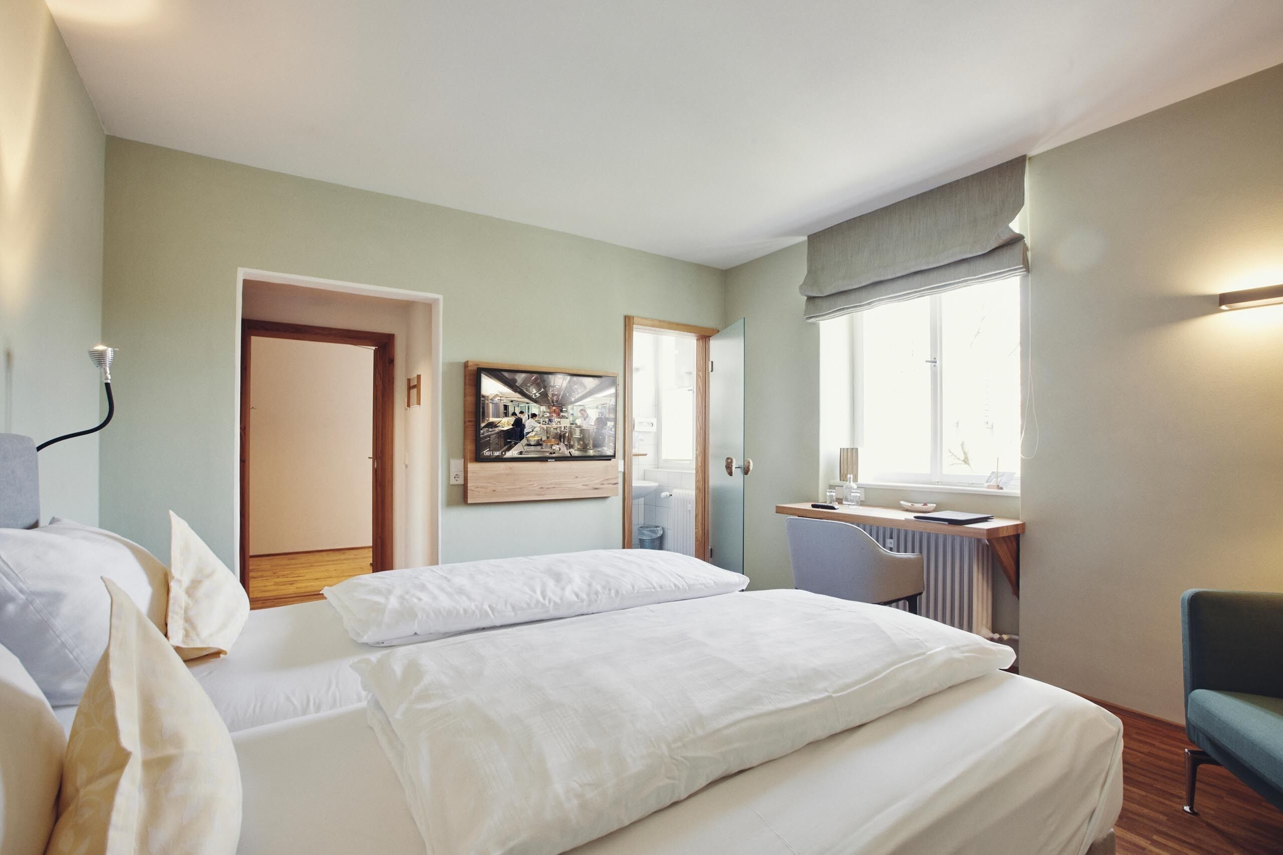 A hotel room with two beds, a desk, a chair, and a window.