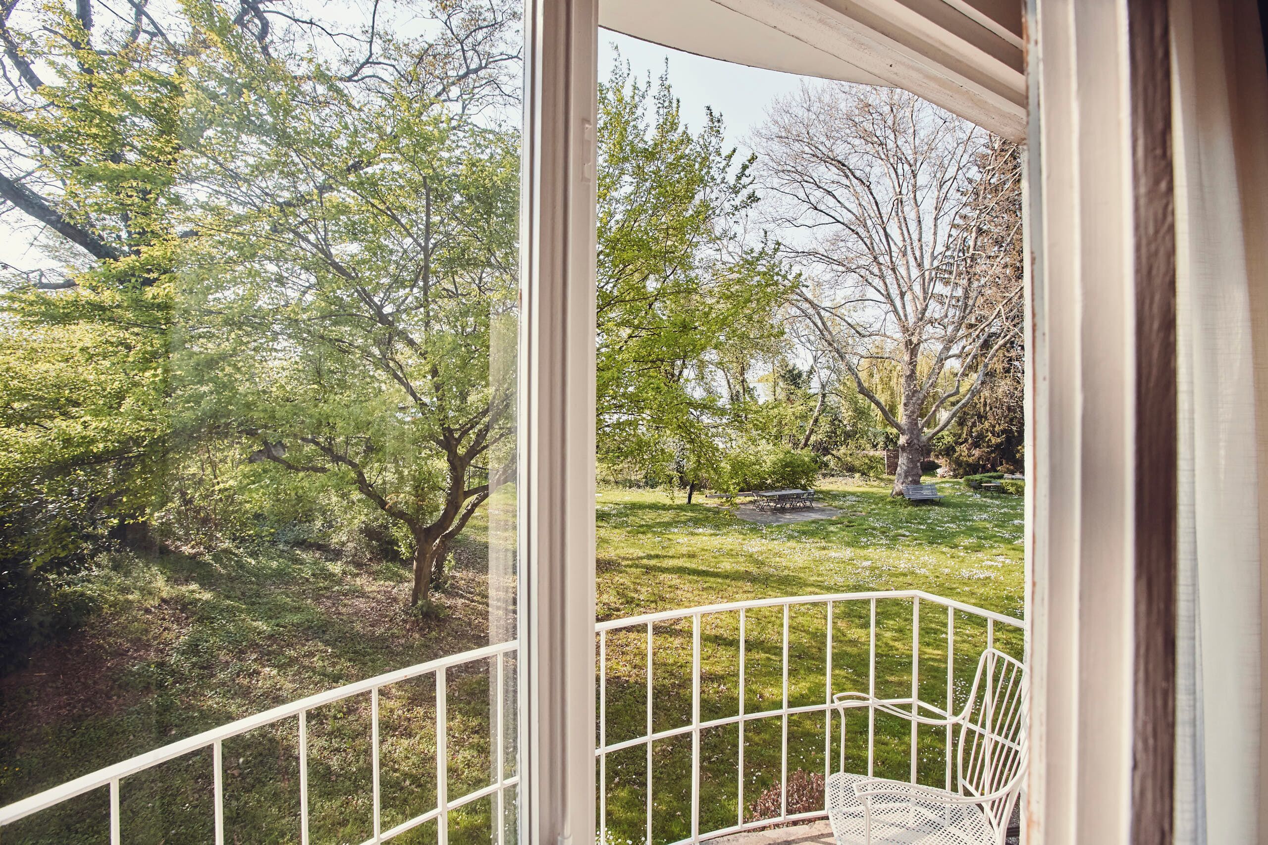 A view from a room with a white metal railing, looking out to a grassy area with trees.