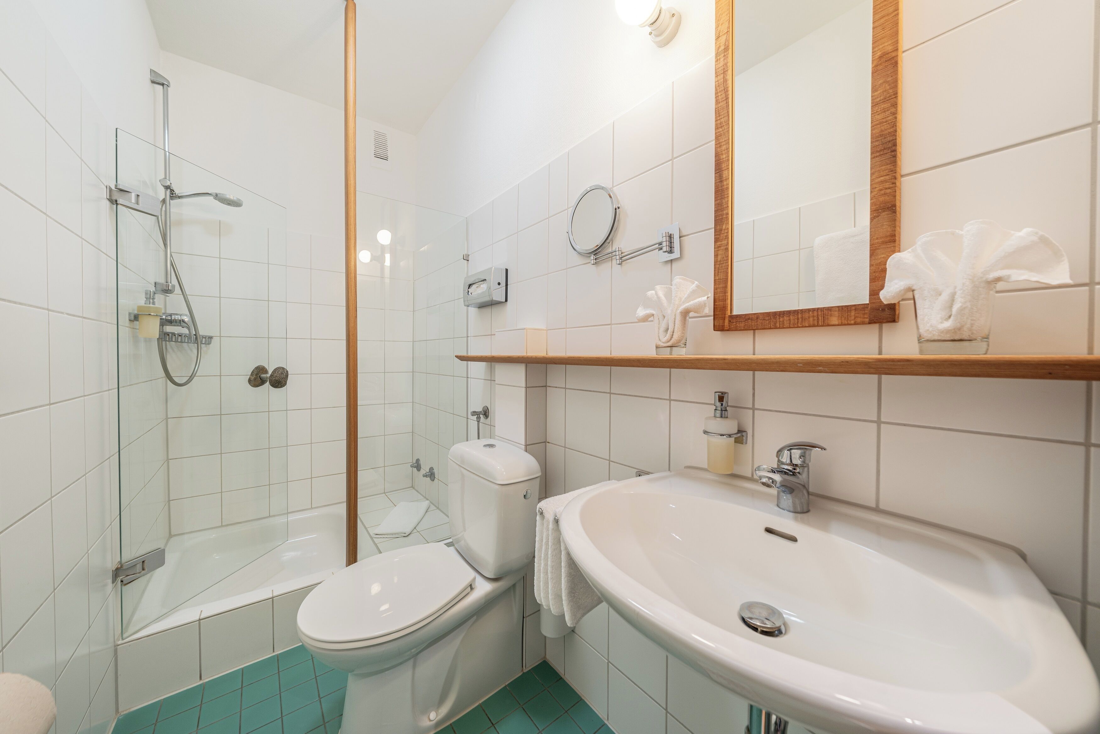 Een badkamer met een douchecabine van glas, een wit toilet en een wastafel met een spiegel erboven.