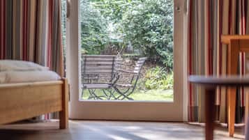 A room with a bed, a wooden table, and a bench outside a door leading to a garden.