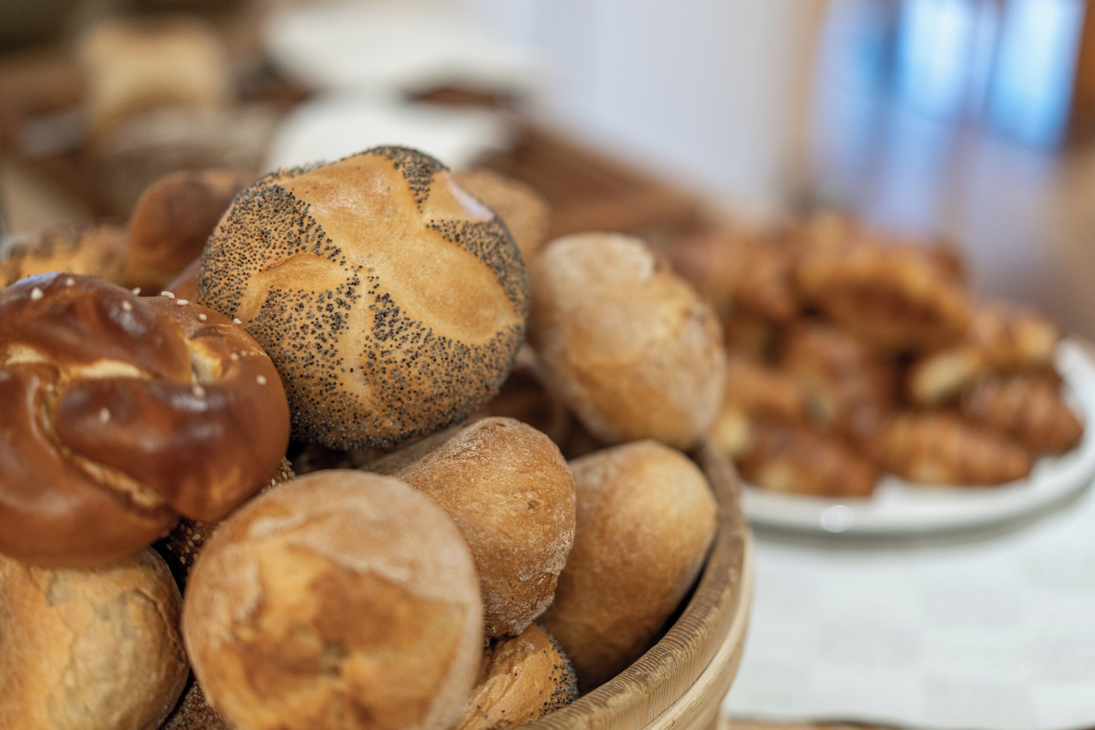 A wooden bowl filled with various types of bread, including poppy-seeded rolls and other baked goods.