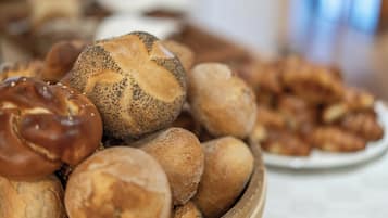 A wooden bowl filled with various types of bread, including poppy-seeded rolls and other baked goods.