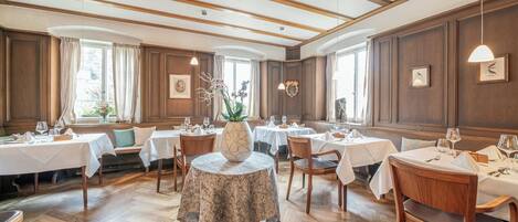 Un comedor con mesas redondas, sillas de madera y un jarrón decorativo en el centro.