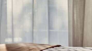Un lit avec une couverture marron et un oreiller gris, partiellement dissimulés par de fins rideaux.