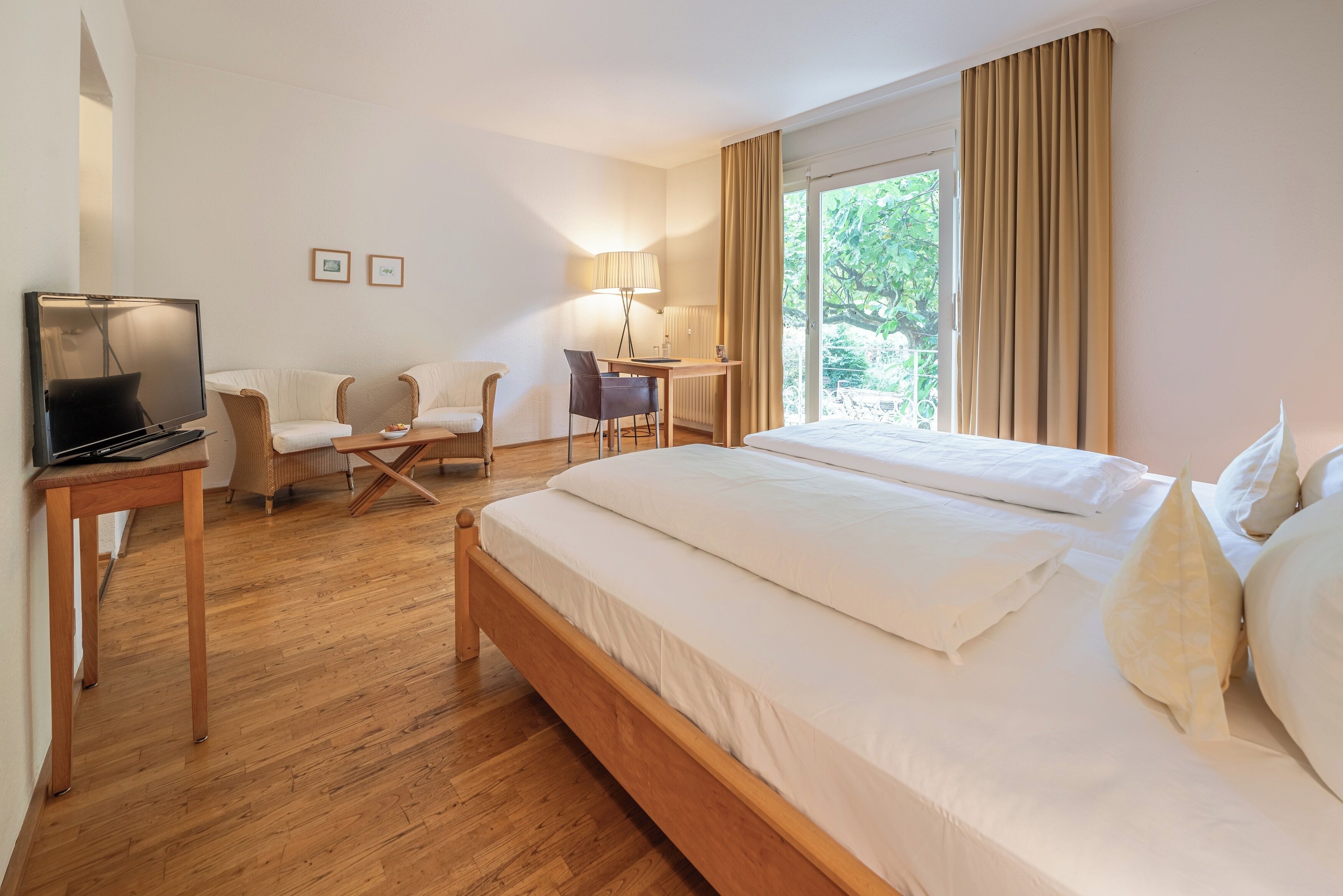 A hotel room with a large bed, a desk with a chair, a TV, and a window with curtains.