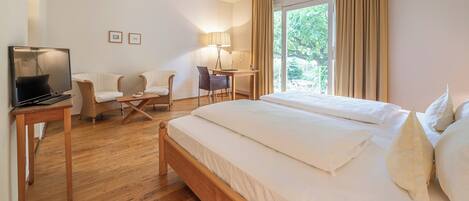 A hotel room with a large bed, a desk with a chair, a TV, and a window with curtains.