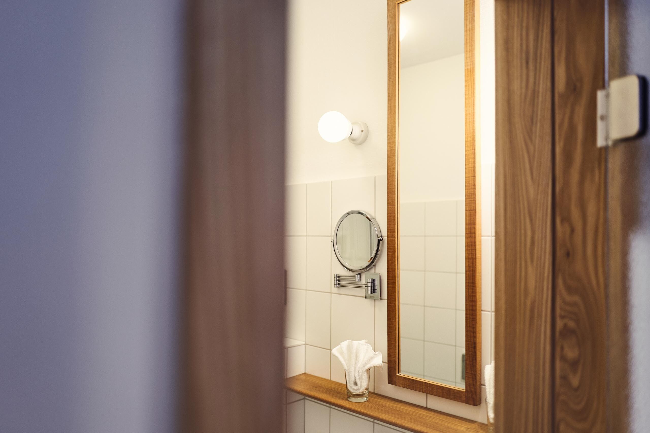A bathroom with a wooden vanity, a round mirror, and a towel dispenser.
