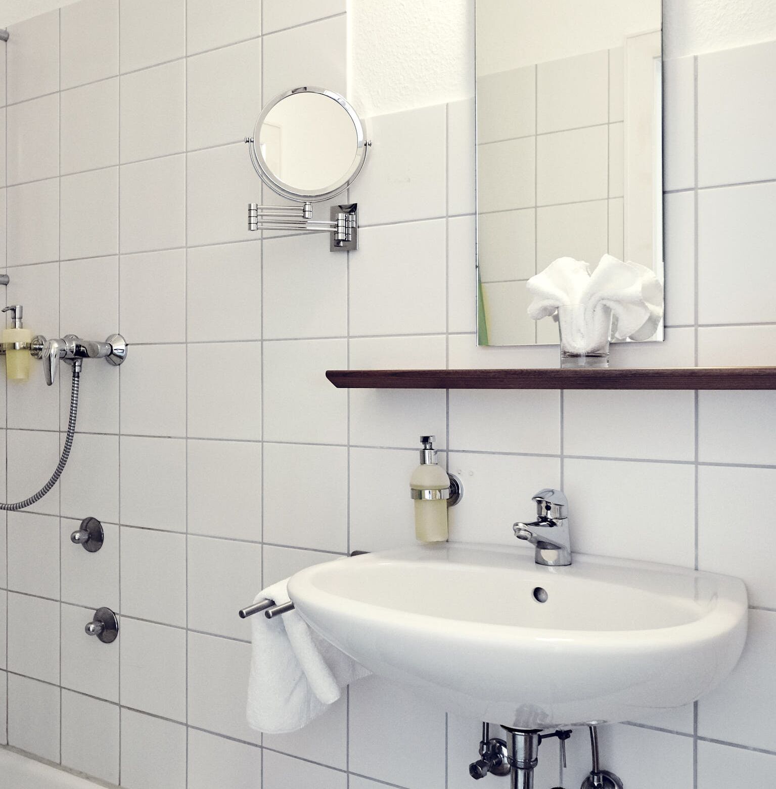 Un baño con lavamanos blanco, un espejo, toallero y ducha.