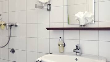 Un baño con lavamanos blanco, un espejo, toallero y ducha.