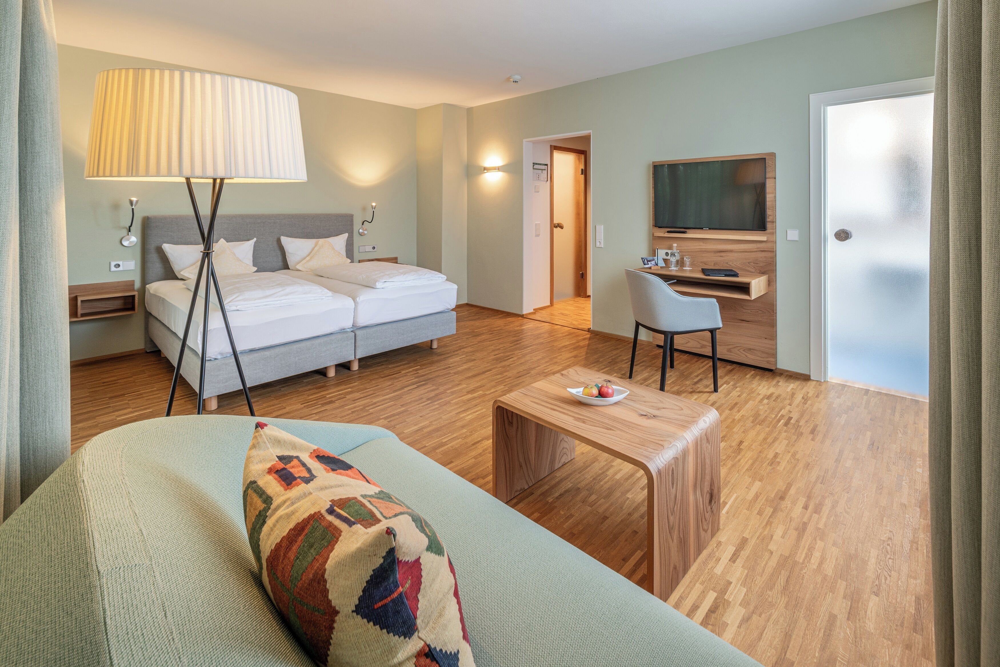 Une chambre d’hôtel moderne équipée d’un lit, d’un canapé, d’une table basse en bois, d’une télévision et d’un bureau avec une chaise.