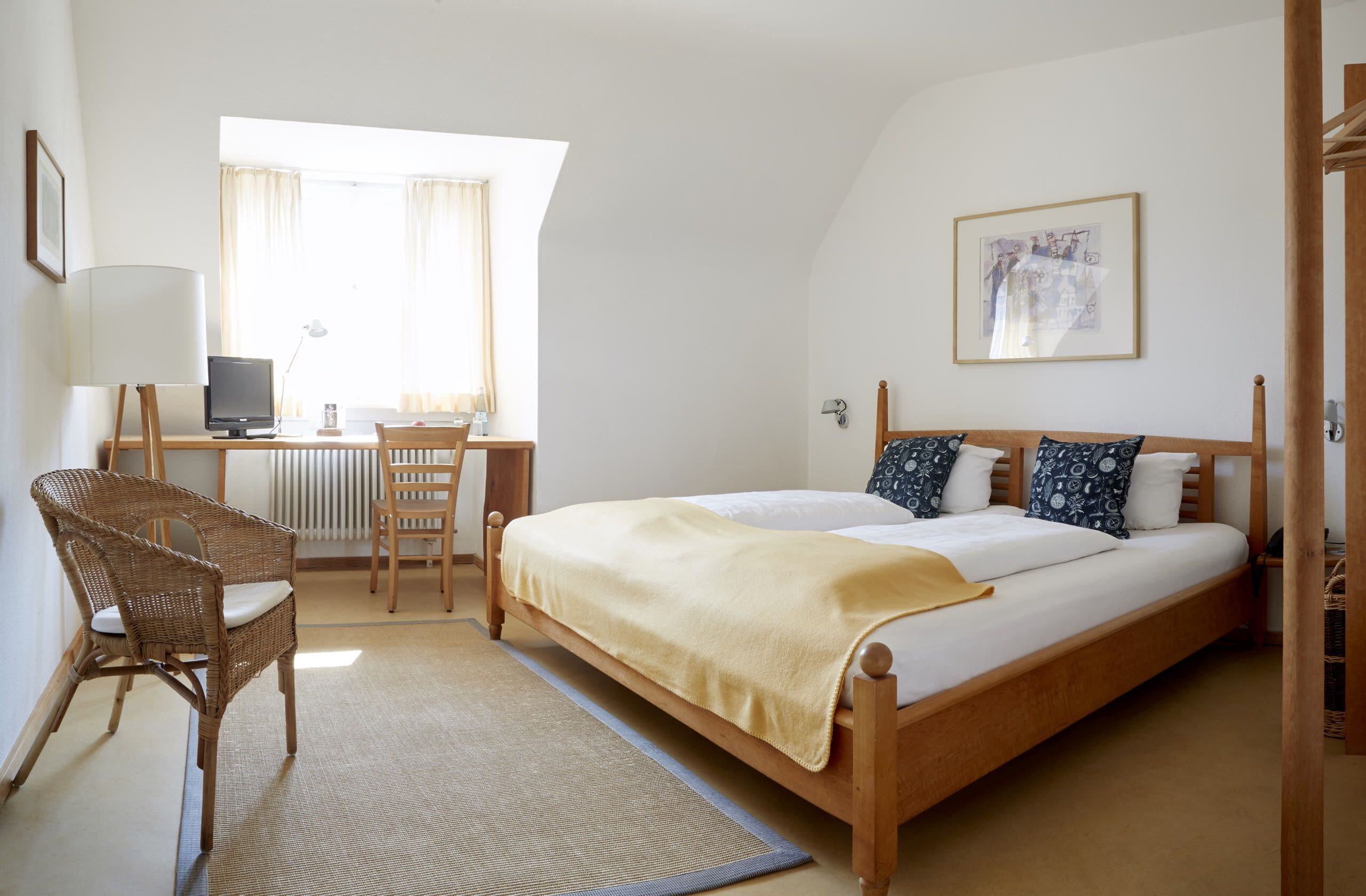 A bedroom with a bed, a desk with a computer, a chair, and a window with curtains.