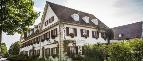 Un hotel tradicional con un estilo arquitectónico europeo clásico, que presenta una fachada simétrica, múltiples ventanas con contraventanas y un letrero destacado que indica que es un hotel.