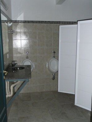 Un bany amb dos orinals, un lavabo amb mirall i una porta blanca.