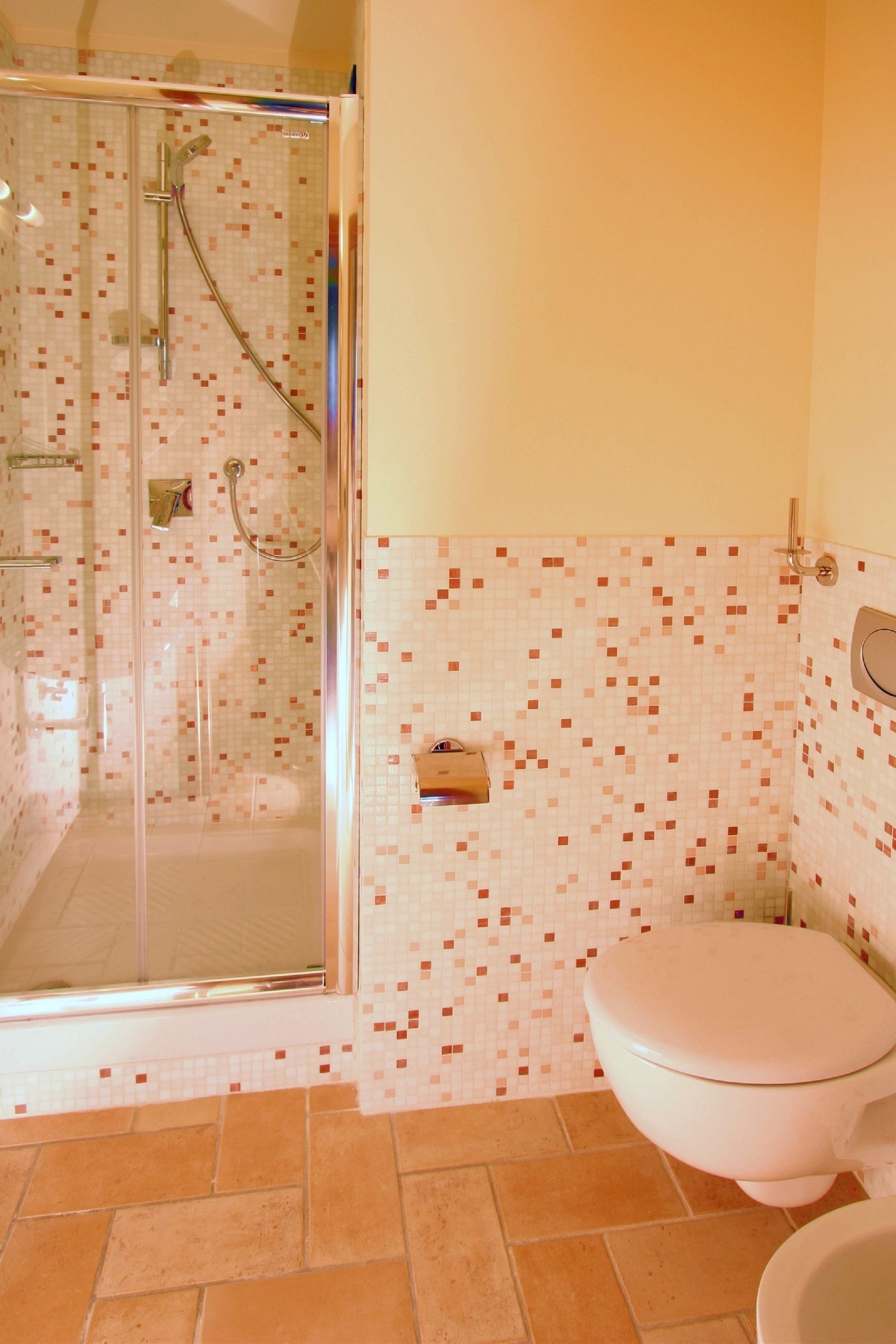 A bathroom with a glass-enclosed shower, a toilet, and tiled walls.