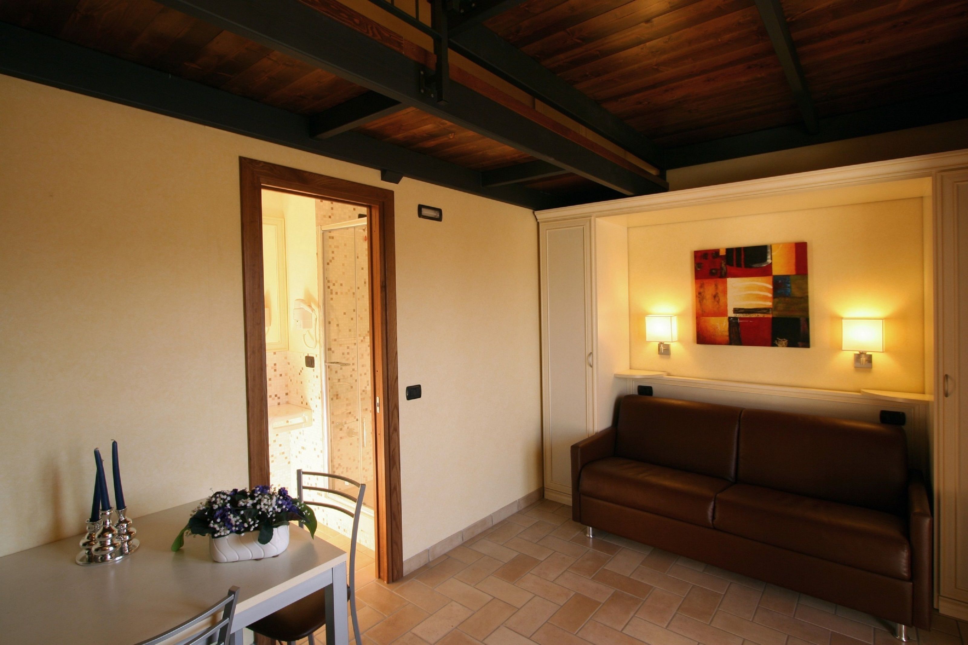 A room with a brown leather sofa, a dining table with candles, and a wall-mounted painting.