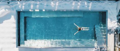 Una piscina exterior con una persona nadando, rodeada de nieve.