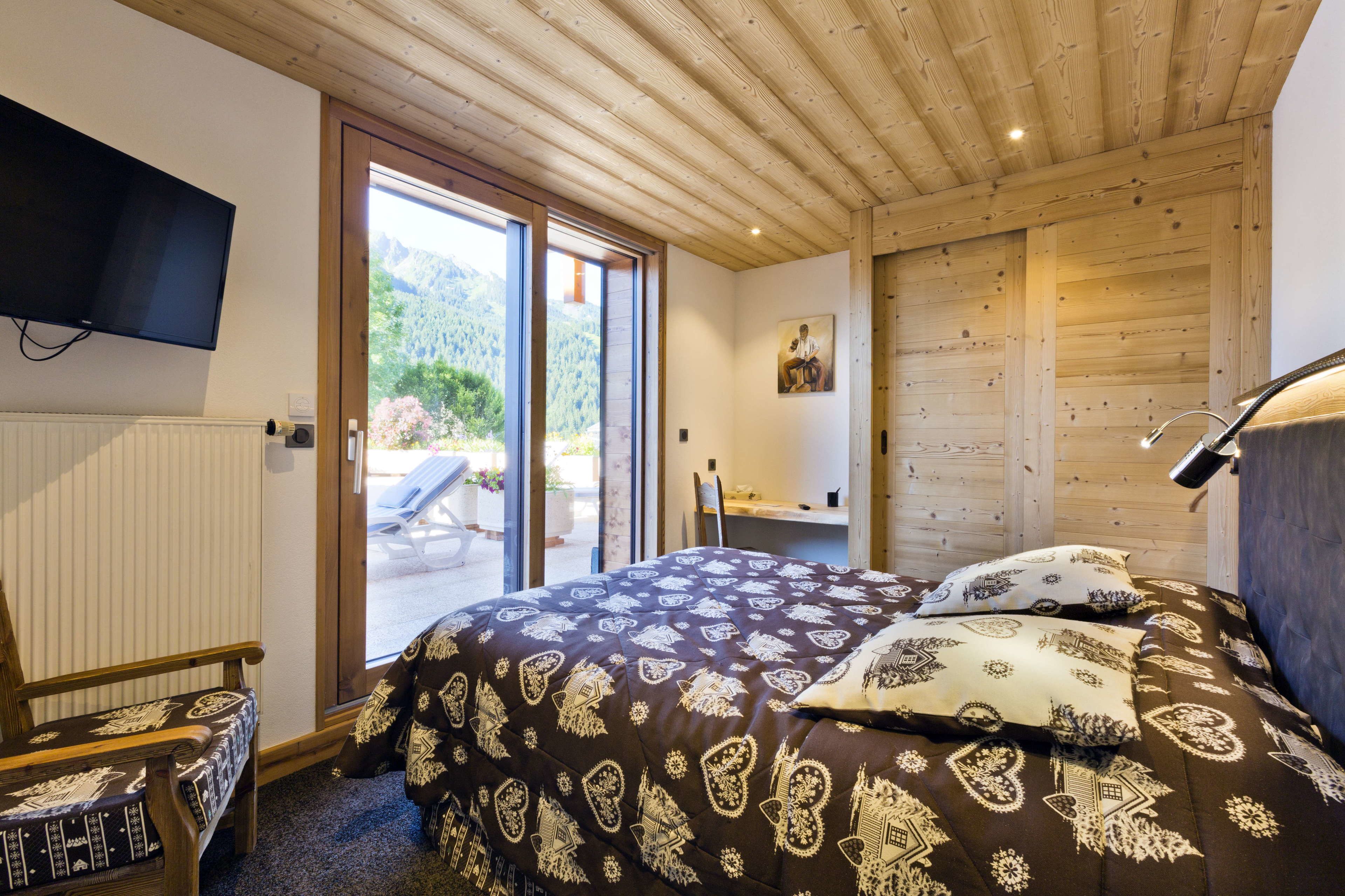 A bedroom with a bed, a chair, a TV, and a sliding glass door leading to a balcony.