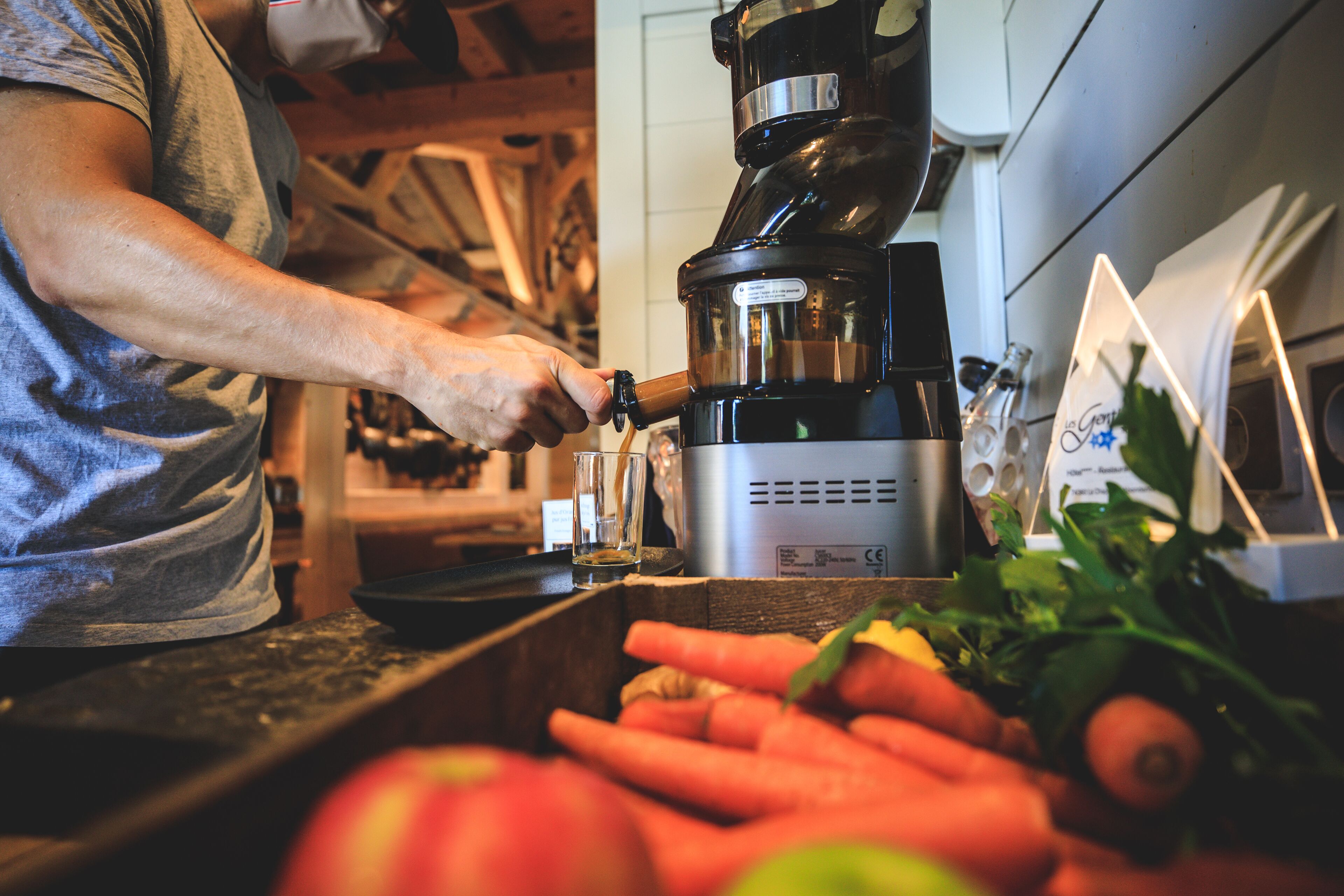 Uma pessoa usando uma máquina de café em uma cozinha com vegetais frescos na bancada.