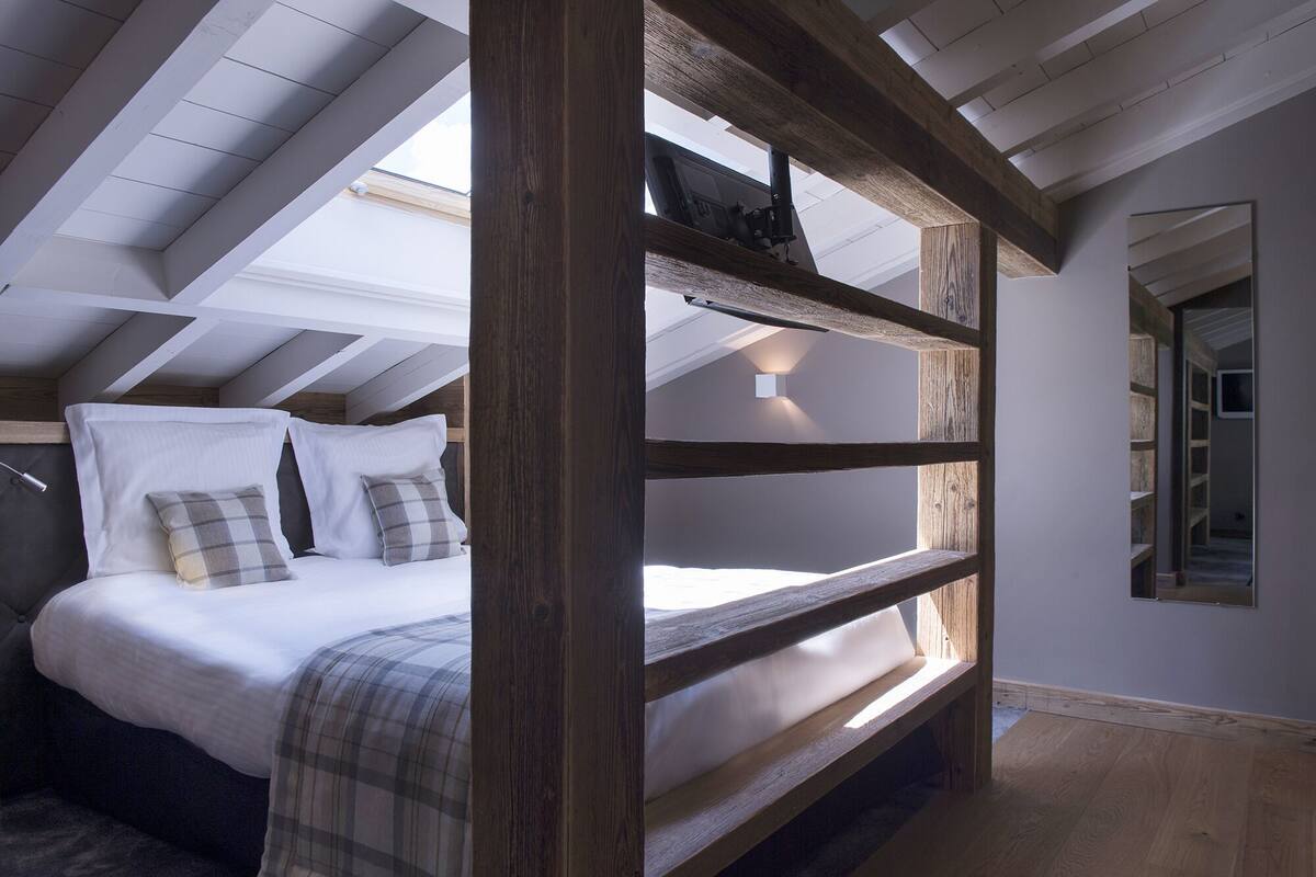 A bunk bed with a wooden frame, a white mattress, and plaid pillows. There is a skylight above the bed, and a mirror on the wall.