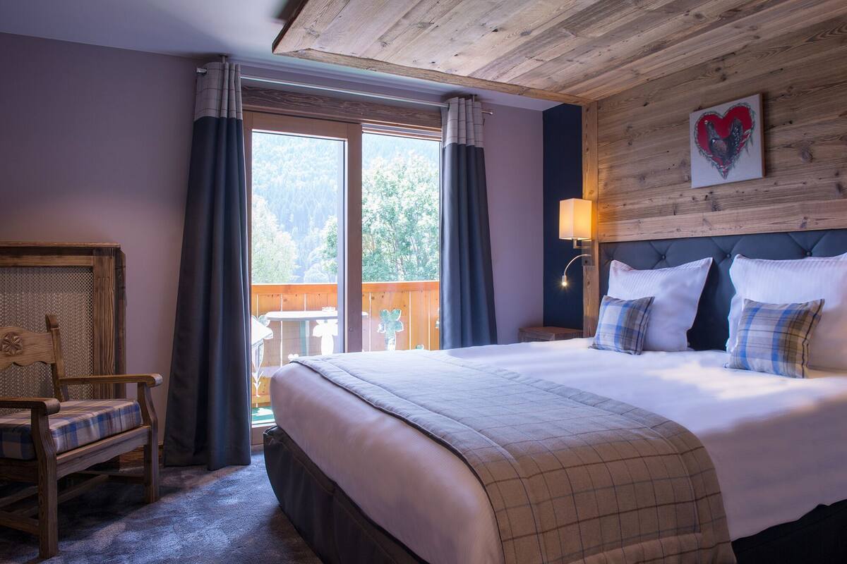 A bedroom with a large bed, a wooden headboard, a nightstand, a chair, and a view of the outdoors.