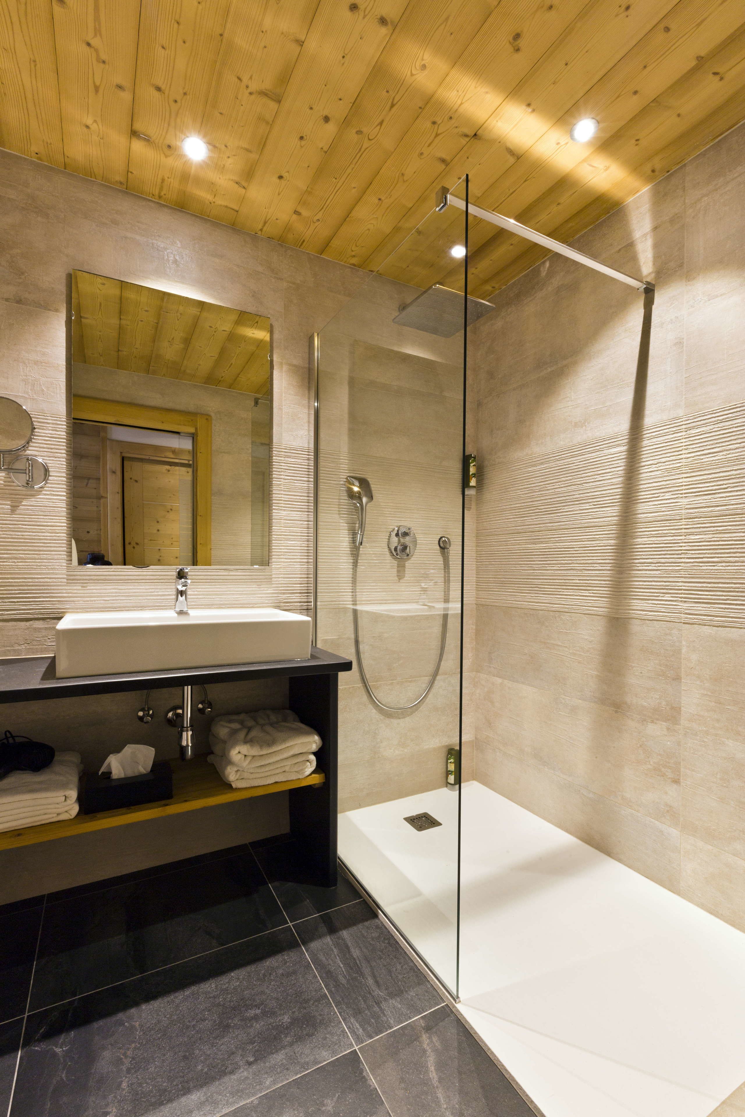 Ein modernes Badezimmer mit Holzboden, einer in Glas eingefassten Dusche, einem weißen Waschbecken und einem Spiegel darüber.