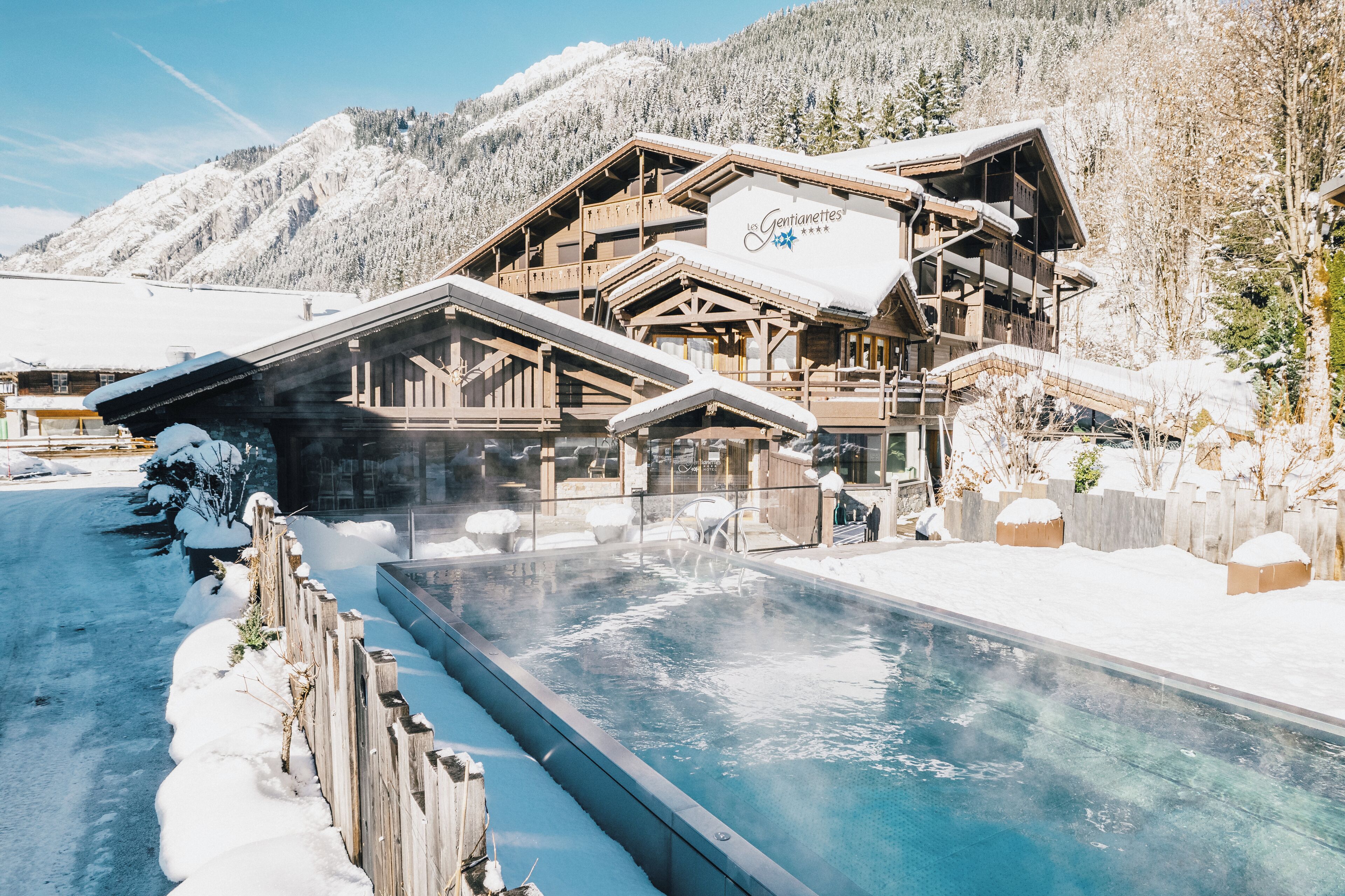Una cabaña de madera con piscina, rodeada de montañas nevadas.