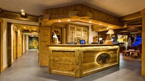 A wooden reception desk with a computer monitor, surrounded by wooden walls and a tiled floor. - Chalet-Hôtel Les Gentianettes, The Originals Relais (Hôtels-Chalets de Tradition) (La Chapelle-d'Abondance)