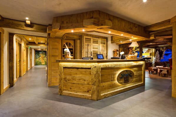 A wooden reception desk with a computer monitor, surrounded by wooden walls and a tiled floor. - Chalet-Hôtel Les Gentianettes, The Originals Collection (Hôtels-Chalets de Tradition) (La Chapelle-d'Abondance)