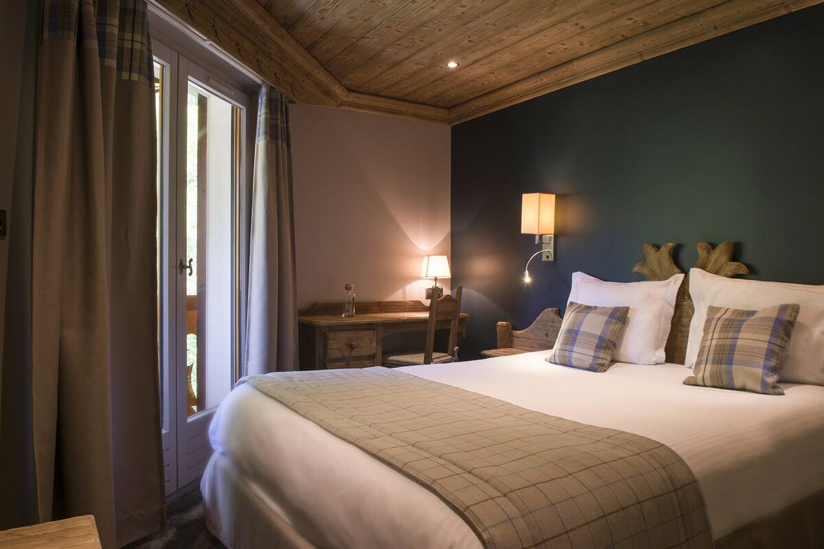 A bedroom with a large bed, a nightstand, a lamp, and a view of the outdoors through a window.