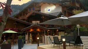 A wooden chalet with a sign reading "Gentianettes" and outdoor seating with umbrellas. - Chalet-Hôtel Les Gentianettes, The Originals Relais (Hôtels-Chalets de Tradition) (La Chapelle-d'Abondance)