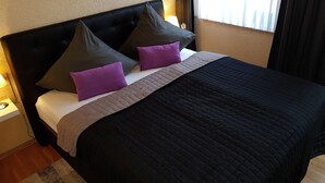 Un lit bien fait, avec une tête de lit noire, deux oreillers et une couverture matelassée.