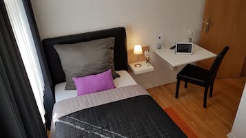 Camera d'albergo con un letto, una scrivania, una sedia, un comodino con una lampada e un tablet.