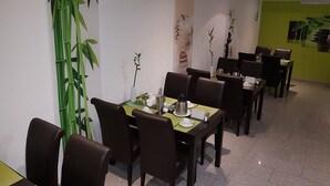 Un espace repas avec des tables dressées pour quatre personnes, des chaises et des plantes décoratives.