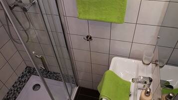 Ett badrum med en dusch som är avskärmad med glasväggar, ett vitt handfat med en grön handduk och en spegel.
