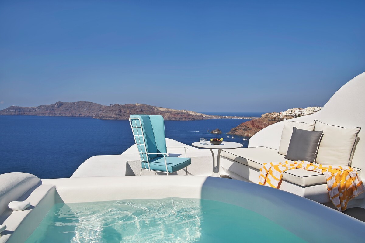 A luxurious outdoor seating area with a white sofa, a blue chair, and a small table with a bowl of fruit.