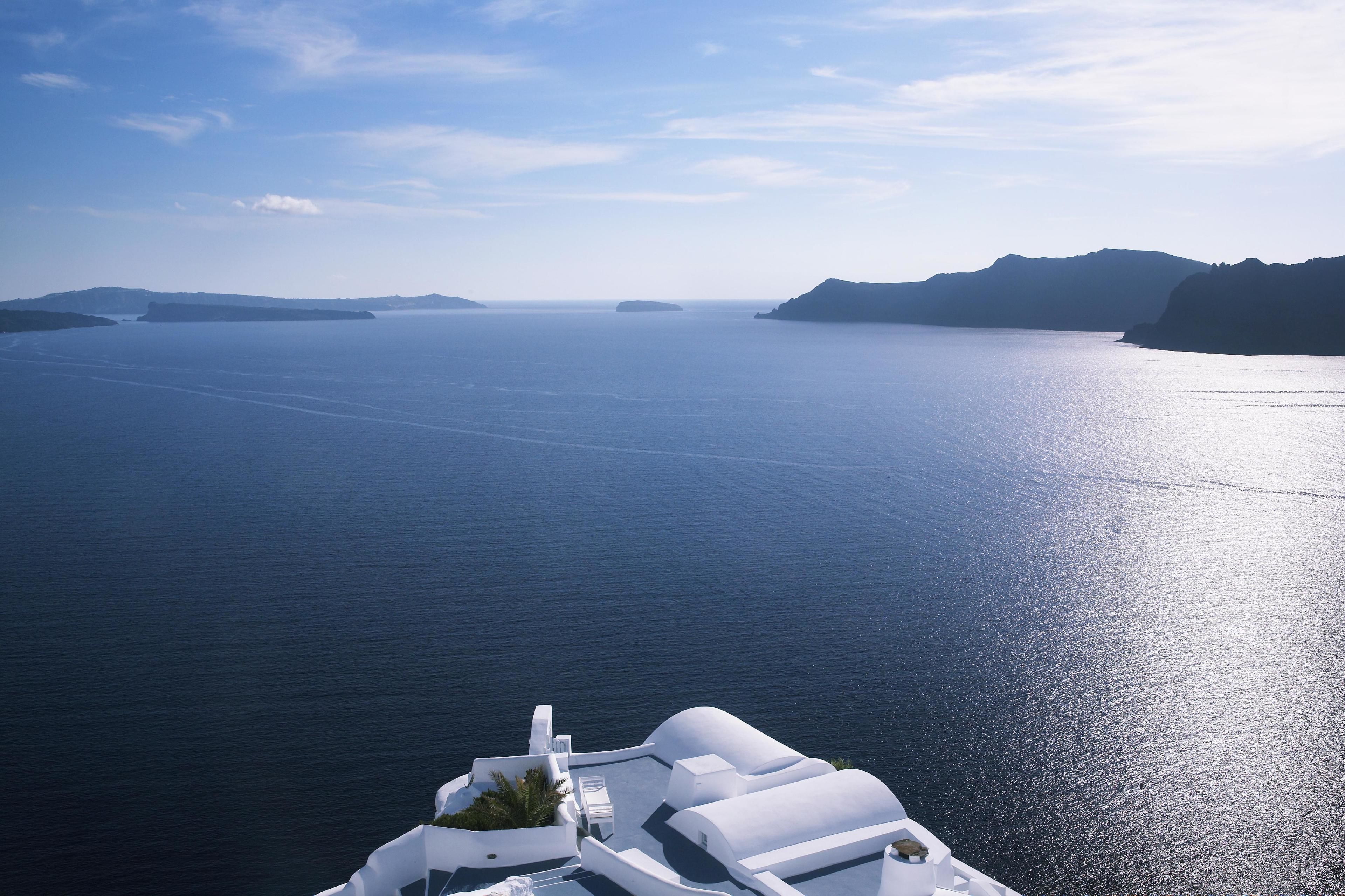 A view of a large body of water with distant landforms, likely a sea or ocean, and a white building with a sloped roof in the foreground.
