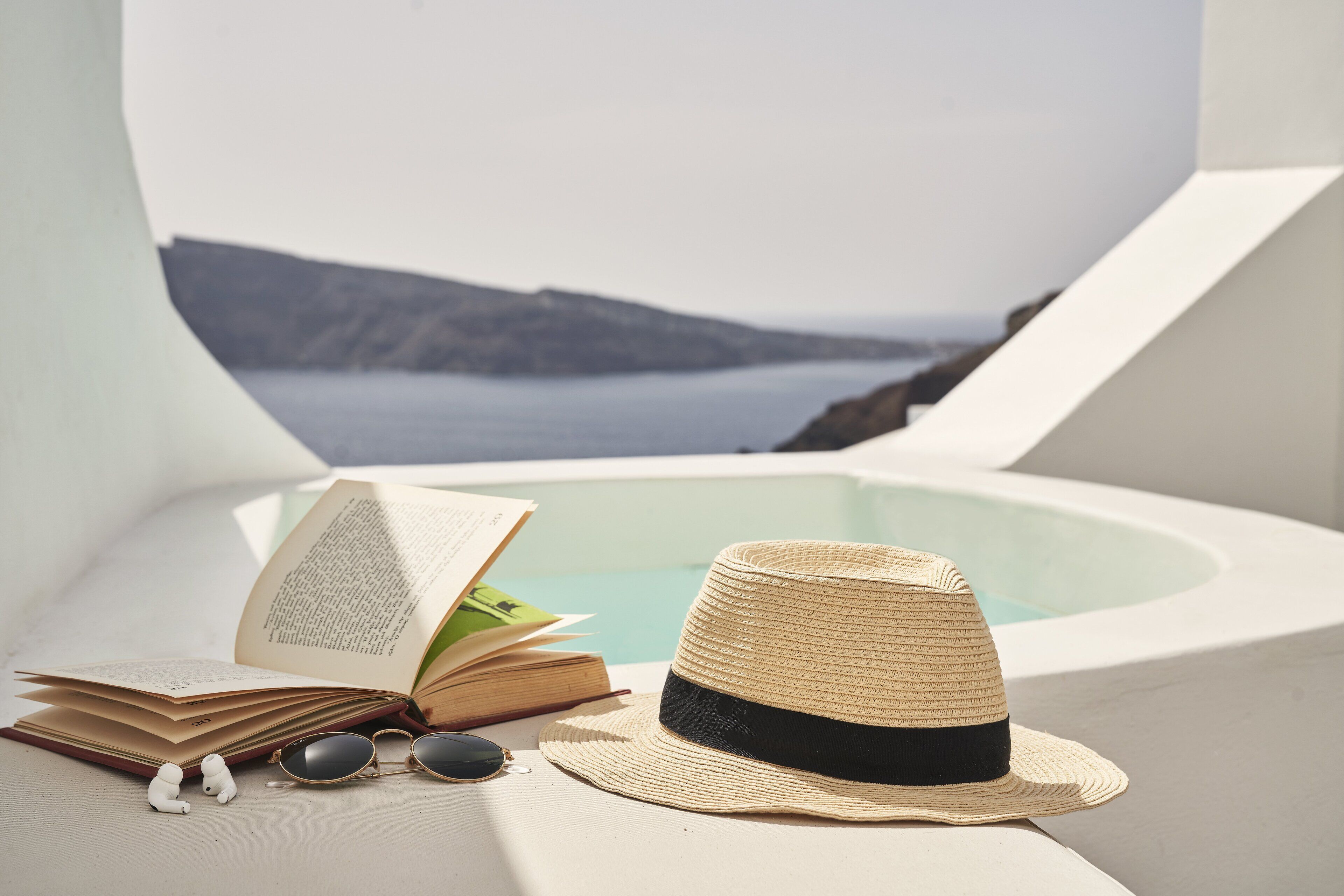 Un libro, gafas de sol y un sombrero de paja en una terraza soleada con vista al mar.