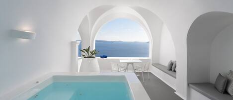 A modern, minimalist bathroom with a large bathtub, a window with a view of the sea, and a small table with chairs.