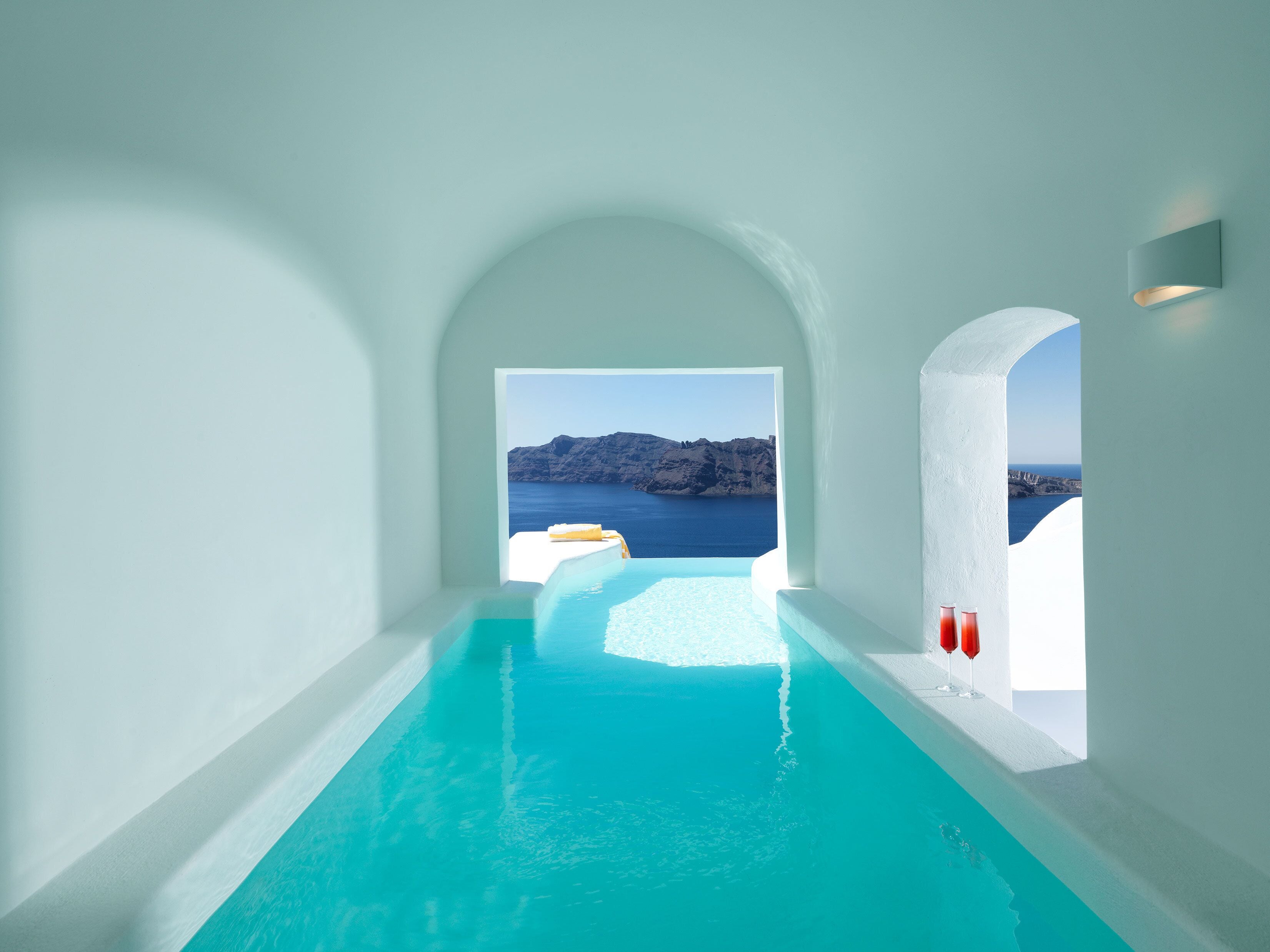A modern infinity pool with clear blue water, leading to a scenic view of the sea and rocky cliffs.