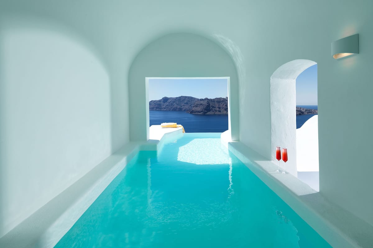 A modern infinity pool with clear blue water, leading to a scenic view of the sea and rocky cliffs.