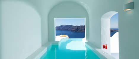 A modern infinity pool with clear blue water, leading to a scenic view of the sea and rocky cliffs.