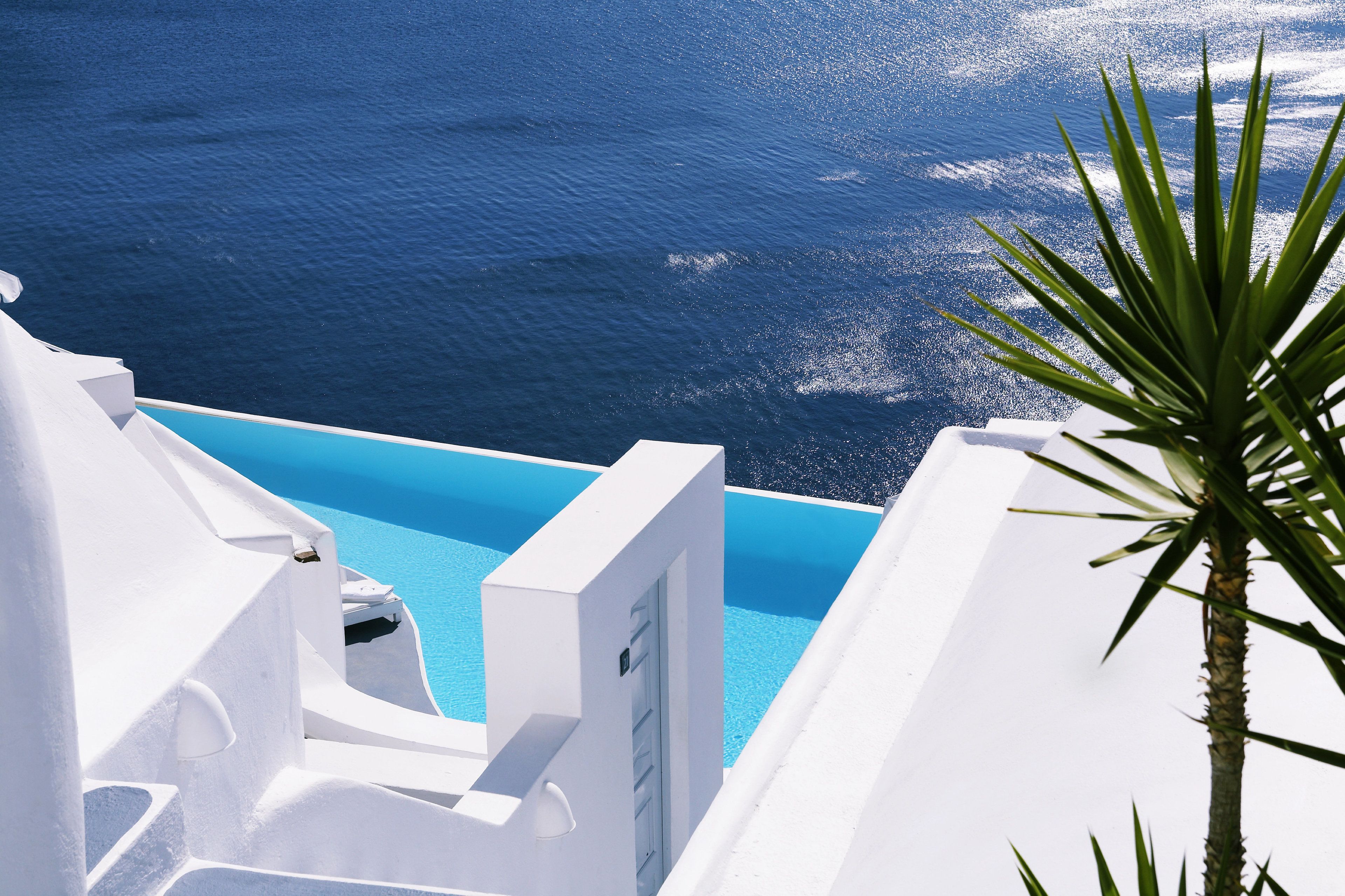 A white building with a pool overlooking a blue sea.