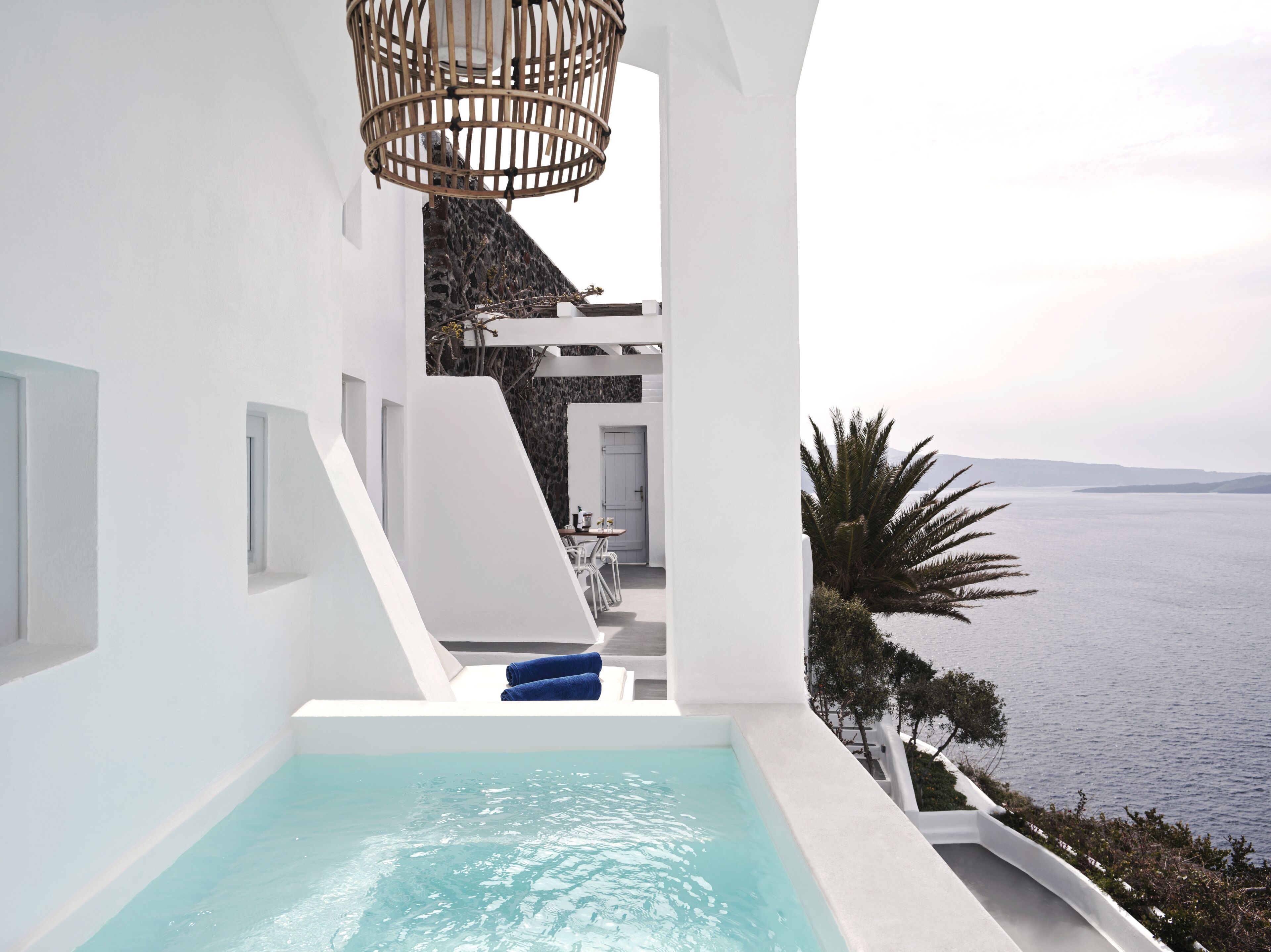 Un espace piscine extérieur moderne avec vue sur la mer, des murs blancs et un luminaire suspendu au plafond en osier.