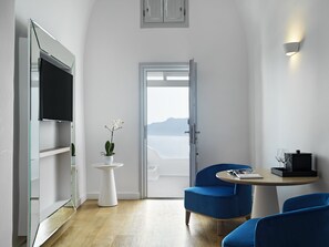 A modern room with a large TV, a small table with a glass, a chair, and a view of the sea through a door. - Katikies Santorini - The Leading Hotels of the world (Santorini)