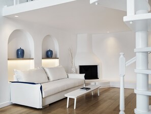 A modern living room with a white sofa, a small white table, and a fireplace. - Katikies Santorini - The Leading Hotels of the world (Santorini)