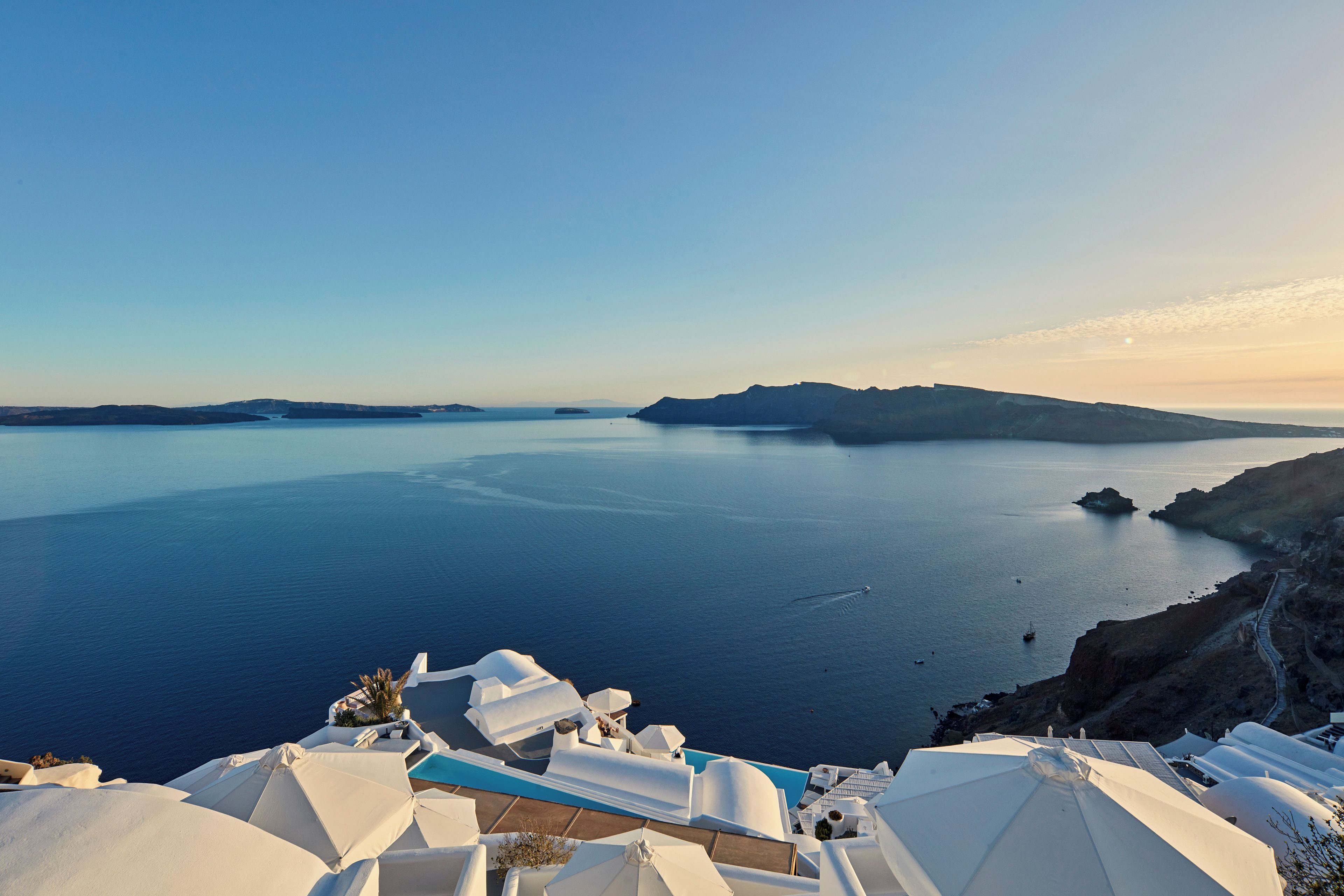 A coastal view with a clear sky, a calm sea, and white buildings with blue roofs.