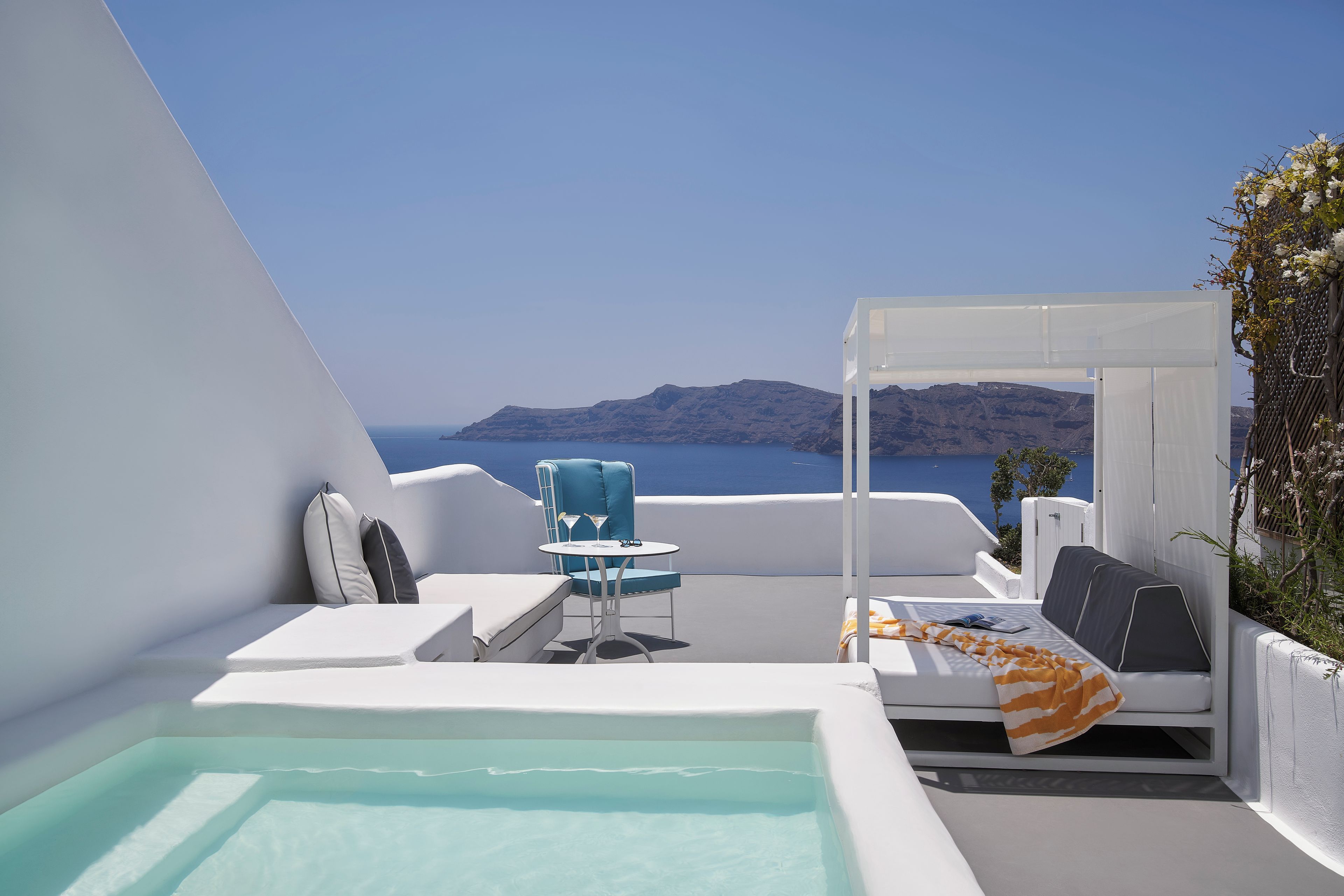 Una terraza soleada con piscina, mobiliario y vista al mar.