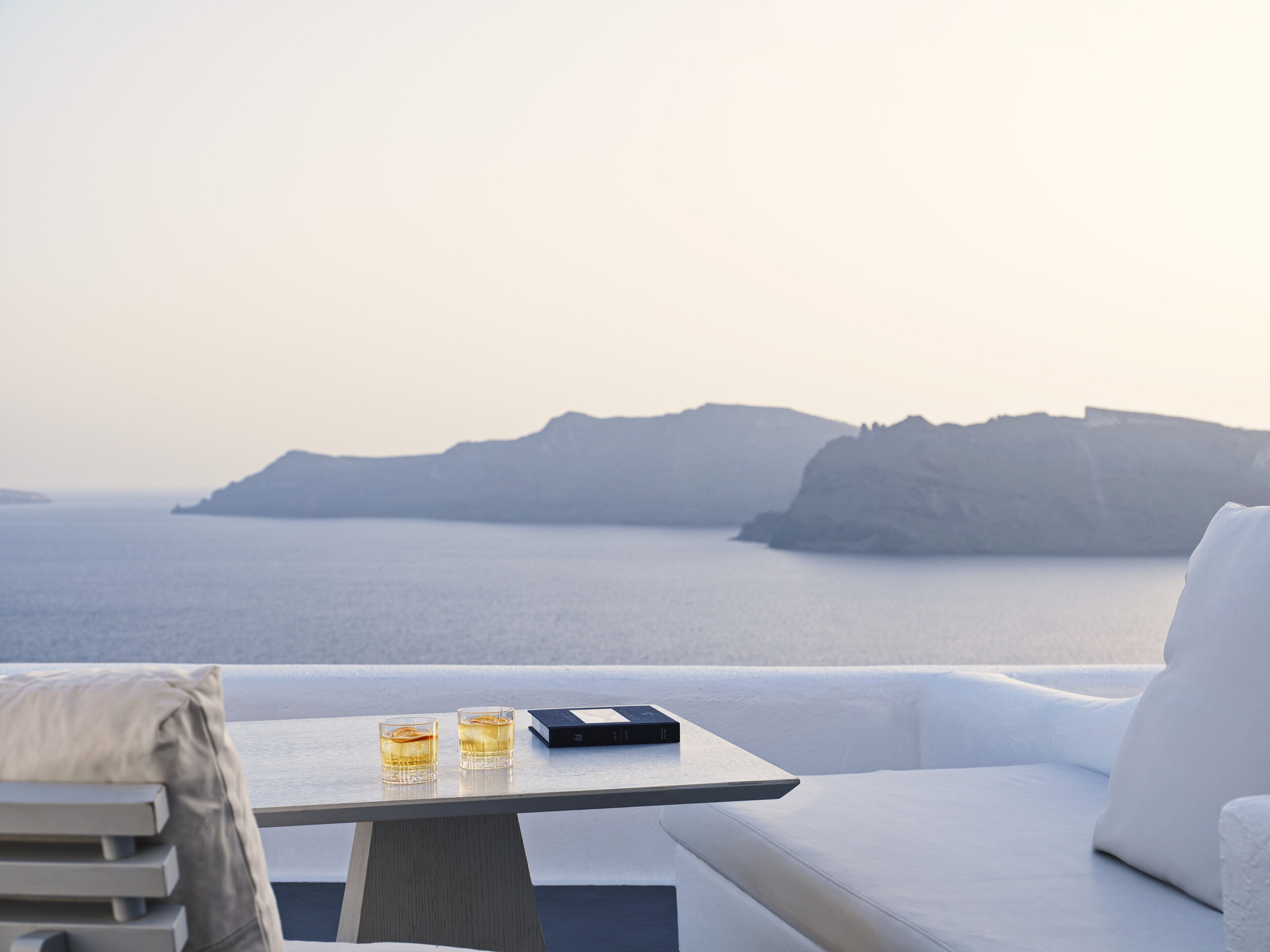 A seaside terrace with a table, two glasses of a beverage, and a book.