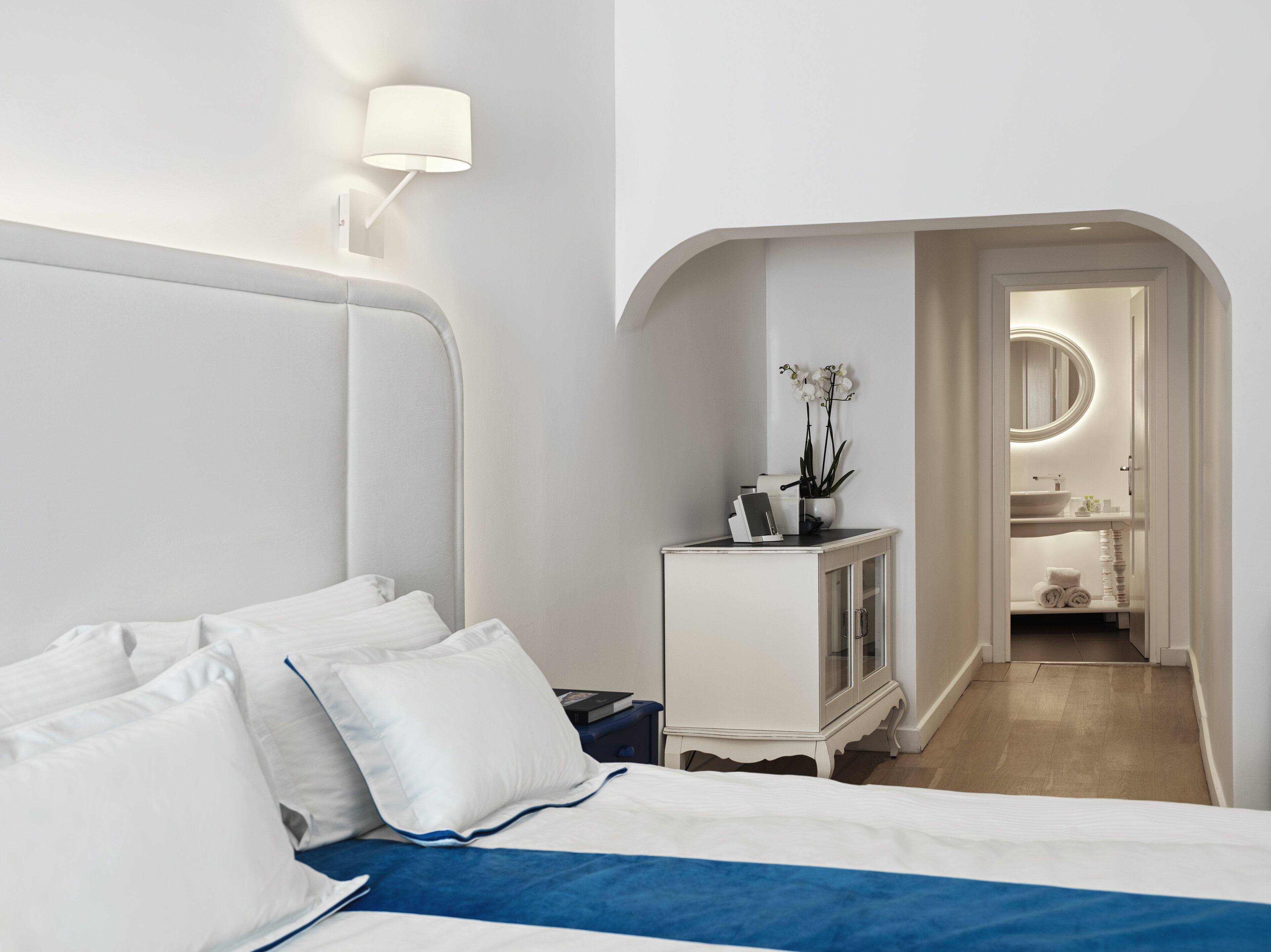Quarto de hotel com uma cama, mesa de cabeceira, abajur e vista para o banheiro.